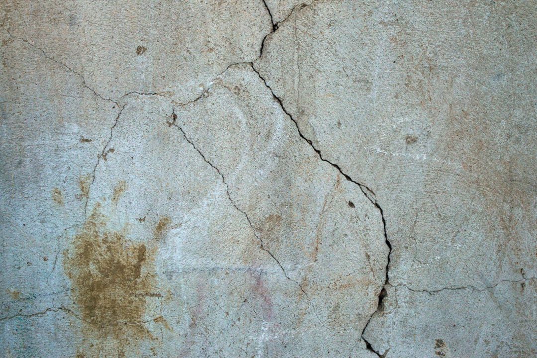 Verzweigter Riss im Außenputz einer Wand mit Feuchtefleck